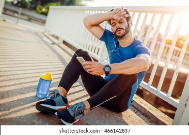 Tired Fitness Man Sweating Taking A Break Listening To Music On Phone After Difficult Training.Fitness,sport,training And Lifestyle Concept.