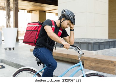 Tired food delivery worker looking exhausted and worried while working riding a bike in the city  - Powered by Shutterstock