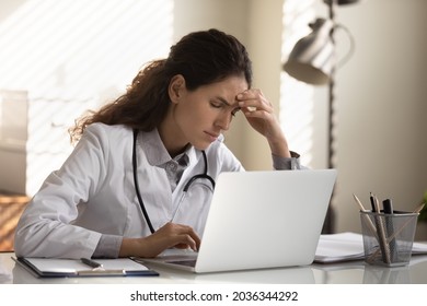 Tired Frustrated Female Doctor Feeling Stress At Workplace, Suffering From Headache, Migraine At Computer. Sick Exhausted General Practitioner Holding Head At Laptop. Medical Profession Problems