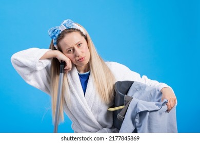 Tired girl cleaned the whole apartment leans with her hand and face on the mop stick holds a bucket of cloths makes a sad face. Effort housewife portrait on blue background. - Powered by Shutterstock