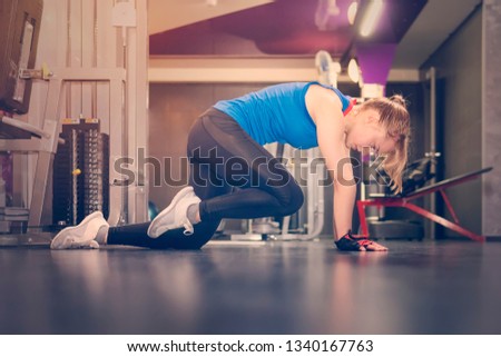 Tired girl portrait with white hair, squatting and pushing to train her legs on leg press machine in modern gym. Healthy lifestyle concept. stretching of the feet. blonde is on her knees