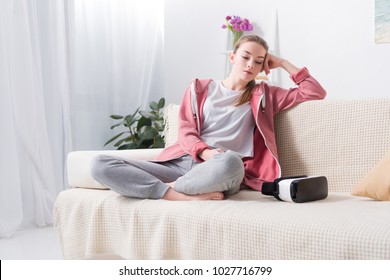 tired girl sitting on sofa and holding smartphone at home