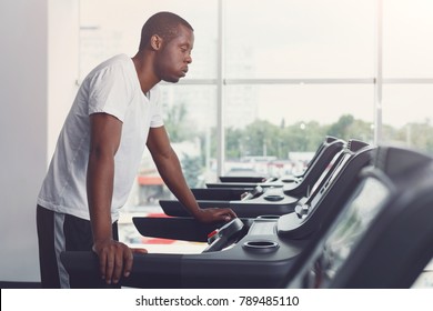 Tired handsome african-american man in fitness club. Cardio workout, running on treadmill. Healthy lifestyle, guy training in gym. Flare effect, copy space - Powered by Shutterstock