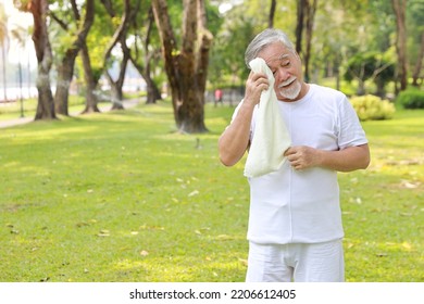 Tired heat and hot asian senior man practice yoga excercise, tai chi tranining and stretching while wipe the sweat away for healthy in park outdoor.  Happy elderly outdoor lifestyle concept