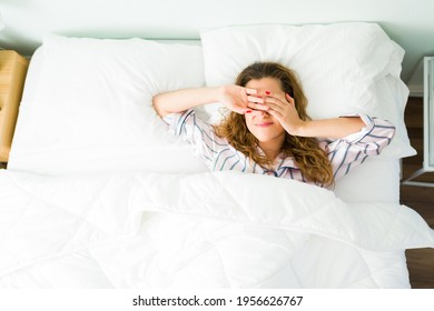 Tired Hispanic Woman Waking Up On Her Bed In The Morning And Covering Her Eyes With Her Hands Because Of The Bright Light