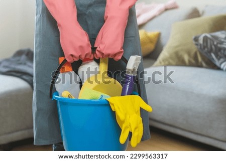 Tired household clean up, housekeeper asian young woman, girl in apron, hand holding bucket of cleaning equipment, cleaning in living room at home. Messy maid or housewife organizing dirty and untidy.