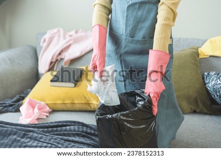 Tired household clean up, housekeeper asian young woman, girl hand holding tissue, napkin paper put in trash bin, cleaning in living room at home. Messy maid or housewife organizing dirty and untidy.