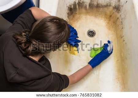 Tired housewife cleaning old dirty bathtub. Exhausted housekeeper rests head on hands holding cleaning tools in bathroom trying to remove dirt, mold and corrosion from bath-tub