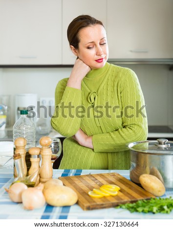 Tired housewife preparing soup with meat at domestic kitchen