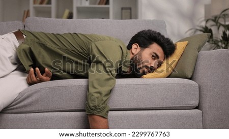 Tired Indian boy slumps on couch feeling listless. Feeling depressed, lack of motivation, sadness, boredom. Exhausted, he collapses on the couch from stress. Burn out.