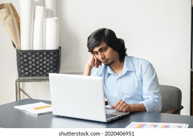 Tired Indian Male Office Employee Staring At The Laptop Screen, Feels Boring And Melancholy. Bored Eastern Man In Smart Casual Shirt Sits At The Desk