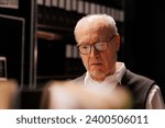 Tired investigator reading confidential federal files, working overhours at criminal case in evidence room. Elderly private detective analzing crime scene report, planning strategy to catch suspect