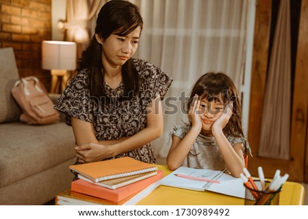 tired kid doing homework in the evening with mother