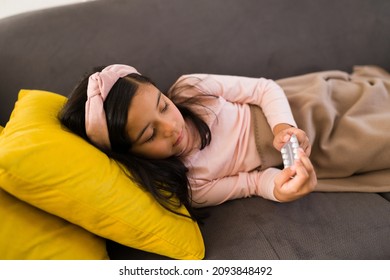 Tired Kid Resting On The Sofa And Covered With A Blanket While Holding A Blister Pack. Sick Girl Taking Medicine Pills