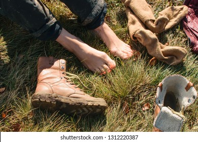 Tired Legs From Trekking. Bare Female Legs On The Grass Next To Dirty Shoes. Rest From A Long Hike.