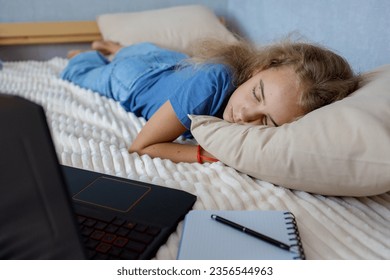 Tired of lessons, a blonde teenage girl sleeps on the bed next to her laptop. The concept of home education and self-study - Powered by Shutterstock