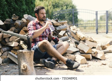 Tired lumberjack sitting and drinking water on bunch of trees - Powered by Shutterstock