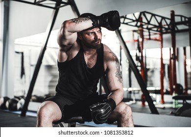 Tired male boxer sitting on stool in gym