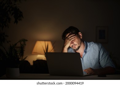 tired male businessman works at home at night on a laptop, works from a home office, studies online,. Internet addiction or a person who works late. a frightened man works late at his home office - Shutterstock ID 2000094419