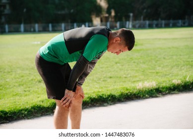 Tired male runner rubbing his forehead while resting after workout, muscular athlete resting after fit training