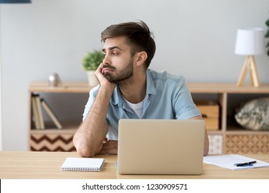 Tired male student or worker sit at home office desk look in distance having sleep deprivation, lazy millennial man distracted from work feel lazy lack motivation, thinking of dull monotonous job