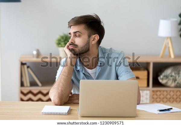 Tired male student or worker sit at home office desk\
look in distance having sleep deprivation, lazy millennial man\
distracted from work feel lazy lack motivation, thinking of dull\
monotonous job