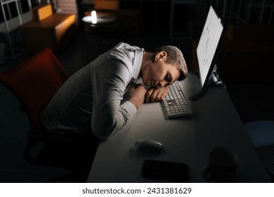 Tired male trader asleep on computer desk late at night alone. Exhausted yougng businessman sleeping with head on keyboard while working overnight on computer. Concept of overwork and deadline. - Powered by Shutterstock