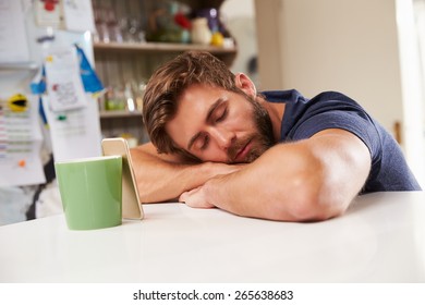 Tired Man Asleep At Kitchen Table Next To Mobile Phone