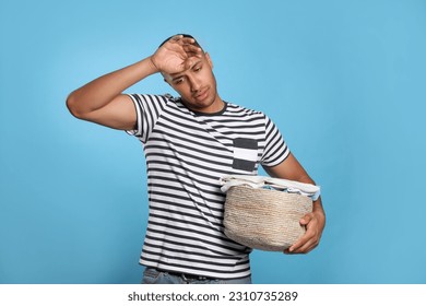 Tired man with basket full of laundry on light blue background - Shutterstock ID 2310735289