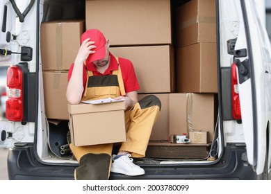 Tired man courier sitting on car with cardboard boxes with documents in his hands