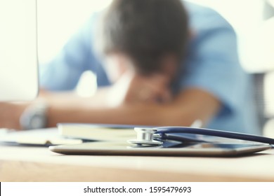 Tired Man Doctor Sleeps Lying On His Hands While Sitting At A Computer Desk. Doctor Works On A Computer In The Clinic After A Night Shift.