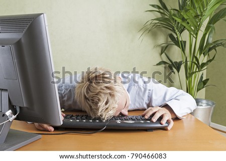 Tired man fallen asleep slumped over computer keyboard when working in office
