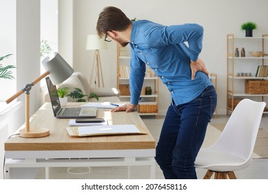 Tired man feels spasm and intense back pain as he stands up after working on computer in sedentary posture for long time. Unhappy stressed young employee has radiculitis or pinched nerve inflammation
