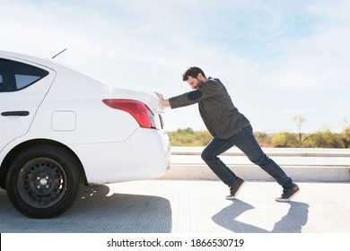Tired man in his 30s trying hard to push his dead car to move it to the side of the road  - Shutterstock ID 1866530719