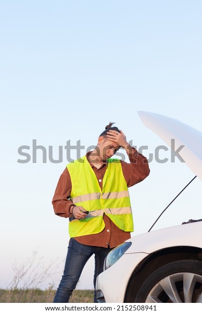 Tired man with problems tries to\
repair a broken car with the open hood and copy space\
around