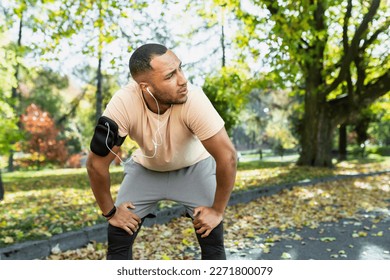 Tired man resting in park after jogging and fitness class, hispanic man using phone listening to music and podcasts in headphones breathing tired and exhausted. - Powered by Shutterstock