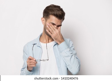 Tired man taking off glasses rubbing dry irritated eyes to relieve pain feeling discomfort suffers eyestrain poor blurry vision isolated on white grey studio background, organ of sight fatigue concept