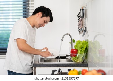 Tired Man Washing Dishes In The Sink In The Kitchen At Home