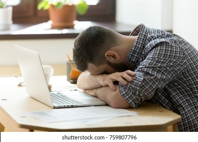 Tired manager falling asleep over laptop in hard working day in home office. Exhausted sleep deprived stressed male worker lying on table and sleeping after overwork, no energy left