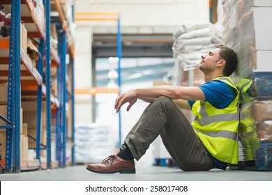 Tired Manual Worker Sitting On Floor In Warehouse