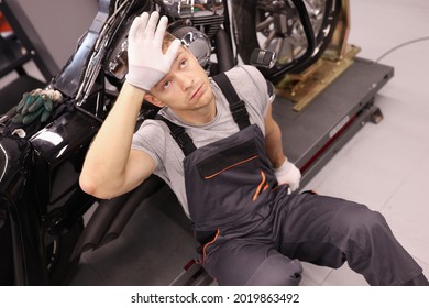 Tired master repairman sitting near motorcycle and holding his head in workshop