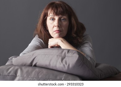 Tired Mature Woman Resting Her Face And Hands Laying Down On Cushions For Comfort While Having Health Care Problems