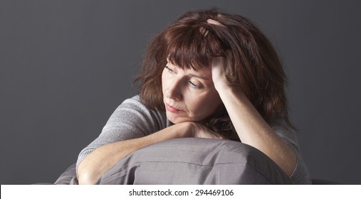 Tired Mature Woman Resting Her Face And Hands Laying Down On Cushions For Comfort While Having Health Care Problems