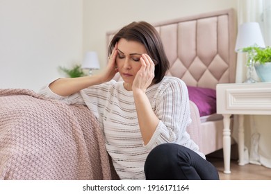 Tired Mature Woman Suffering From Headache, Migraine, Female Sitting At Home On The Floor, Holding Her Head With Her Hands