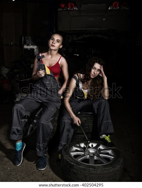 tired mechanics sexy girls sitting on a pile\
of tires on a car repairs and smoke, one of the girls holding a\
wrench in his hand. colorless life\
concept