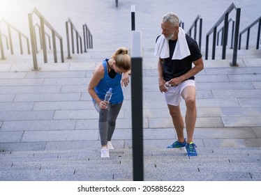 Tired Middle Aged Couple, Man And Woman In Sportswear Walking Up The Stairs After Exercising Together Outdoors