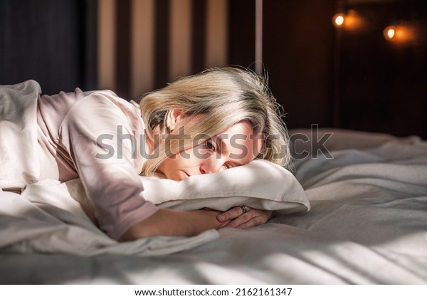 Tired middle aged woman lying in bed can\'t sleep\
late at morning with insomnia. Adult lady sick or sad depressed\
sleeping at home.\
