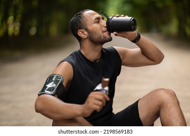 Tired middle eastern young guy sportsman sitting on the ground at public park, having snack while training outdoors, drinking protein cocktail and eating protein bar, copy space. Sports nutrition - Powered by Shutterstock