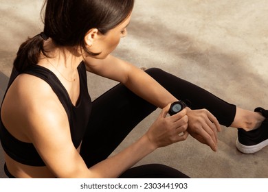 Tired millennial european woman athlete in sportswear checks pulse on fitness tracker in city, outdoor. Result body care, cardio training and fitness, gadget for active workout