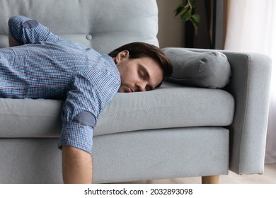 Tired Millennial Guy In Casual Sleeping At Daytime Due To Overwork, Fatigue, Stress, Sleepless Night. Lazy Sleepy Bored Guy Lying On Couch With Closed Eyes, Relaxing At Home. Energy Recreation Concept